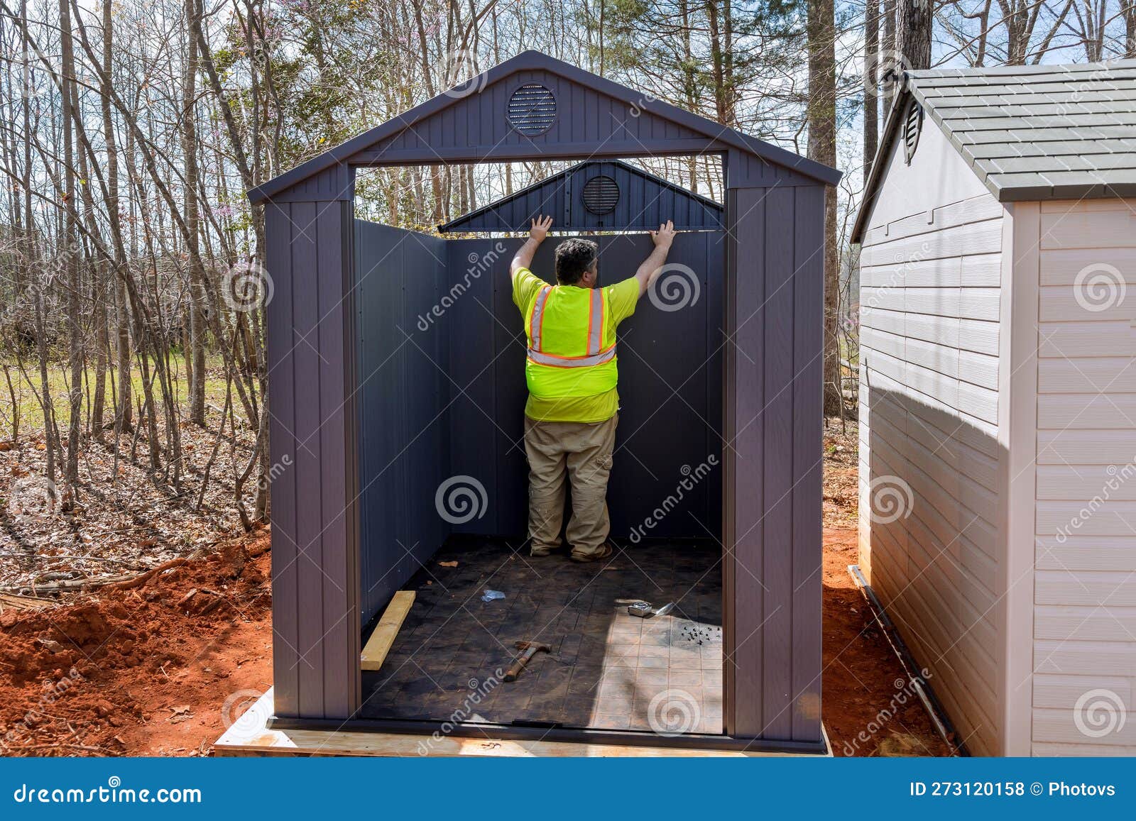 A Worker Assembles a Plastic Vinyl Storage Shed in the Backyard of a