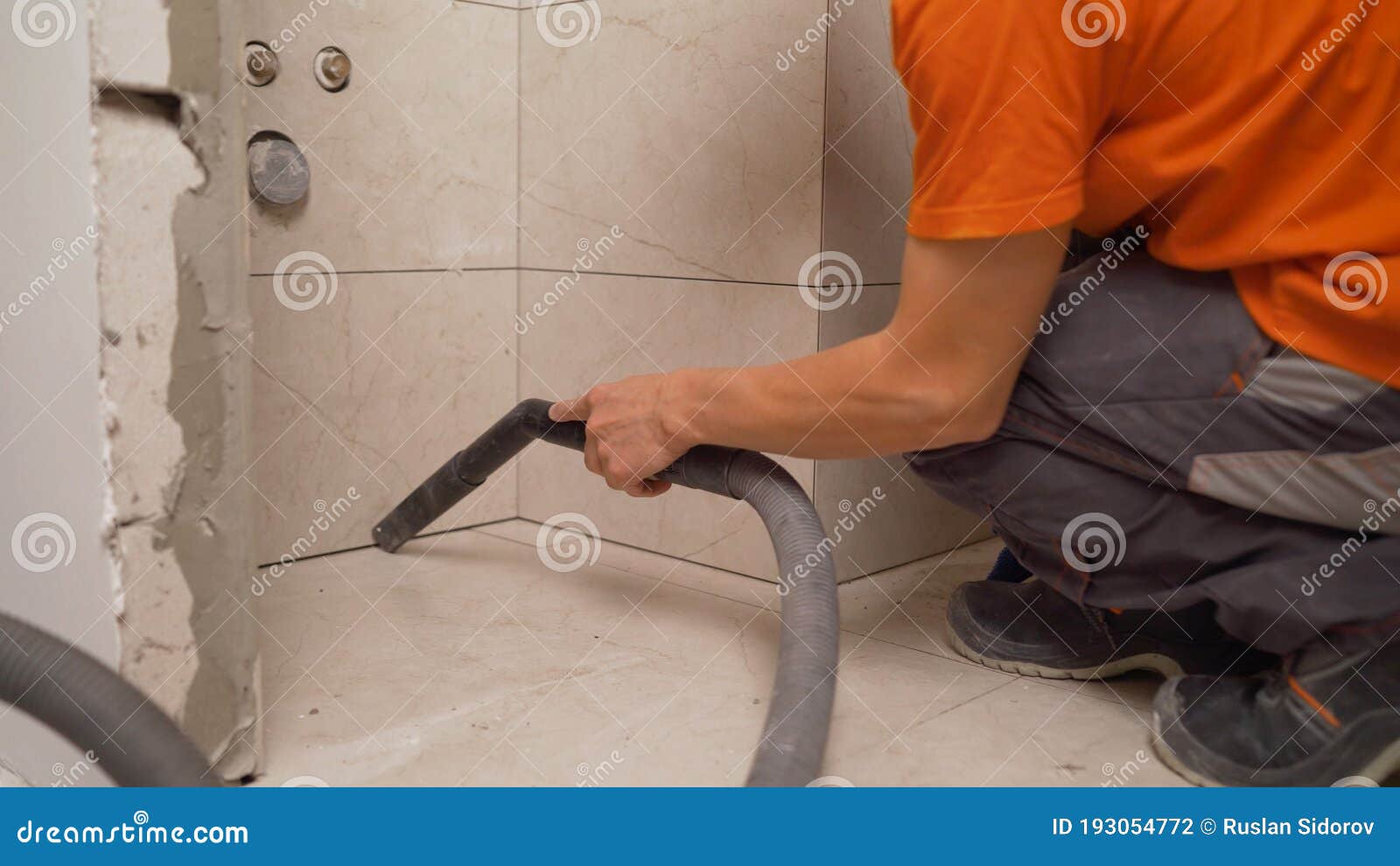 Worker Cleans Seams between Tiles Using a Vacuum Cleaner. a Worker Vacuums the Floor Tiles Stock