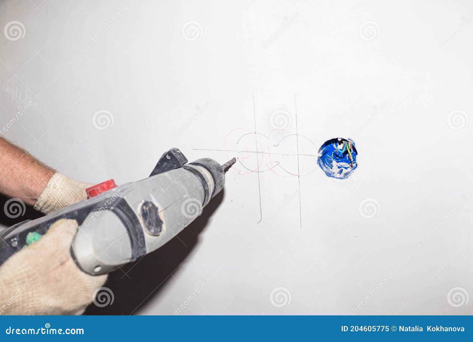 A Worker with a Drill Drills a Wall. Additional Electrical Outlet in