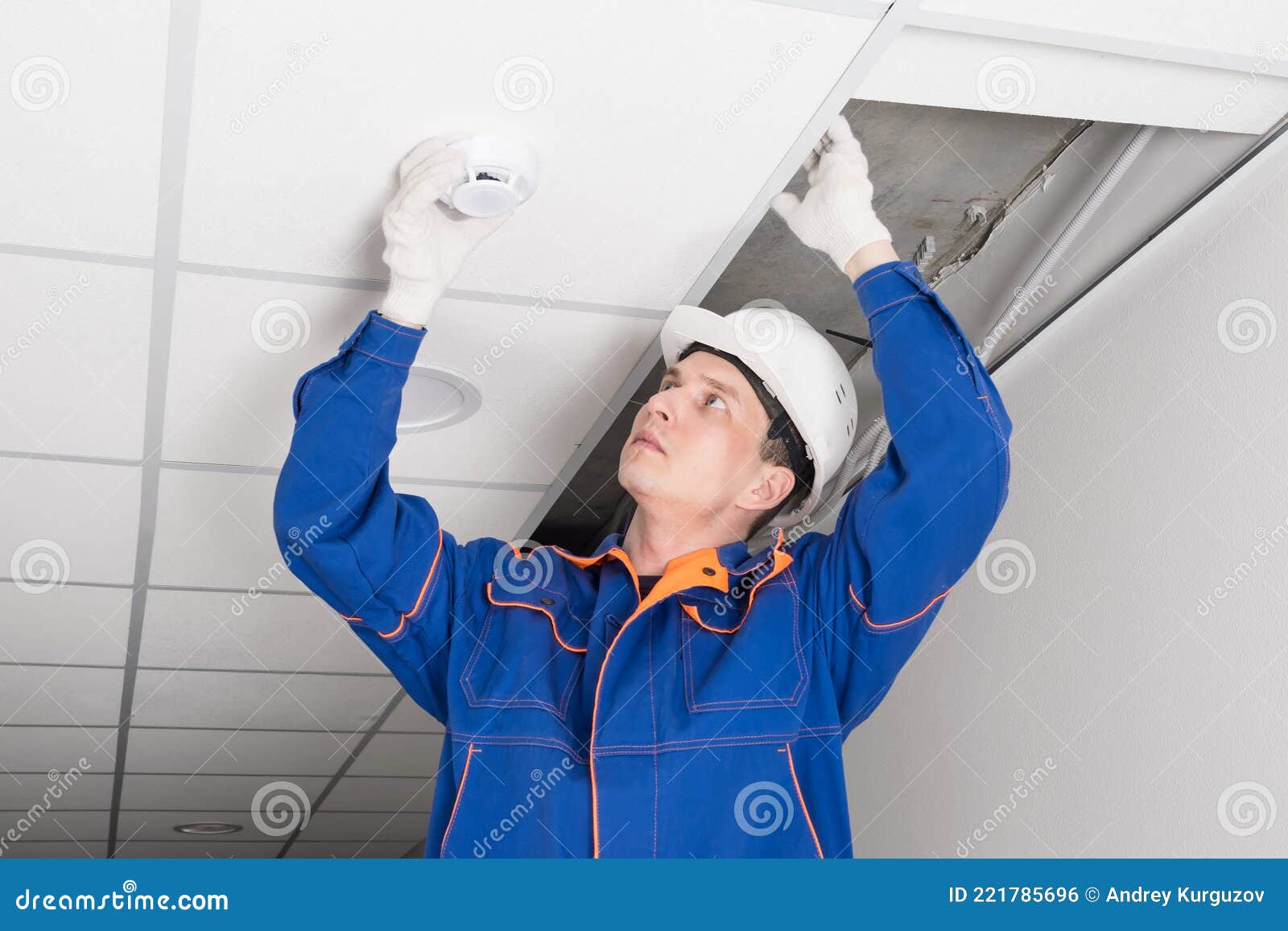 A Worker Installs a Smoke and Fire Detector on the Ceiling in the