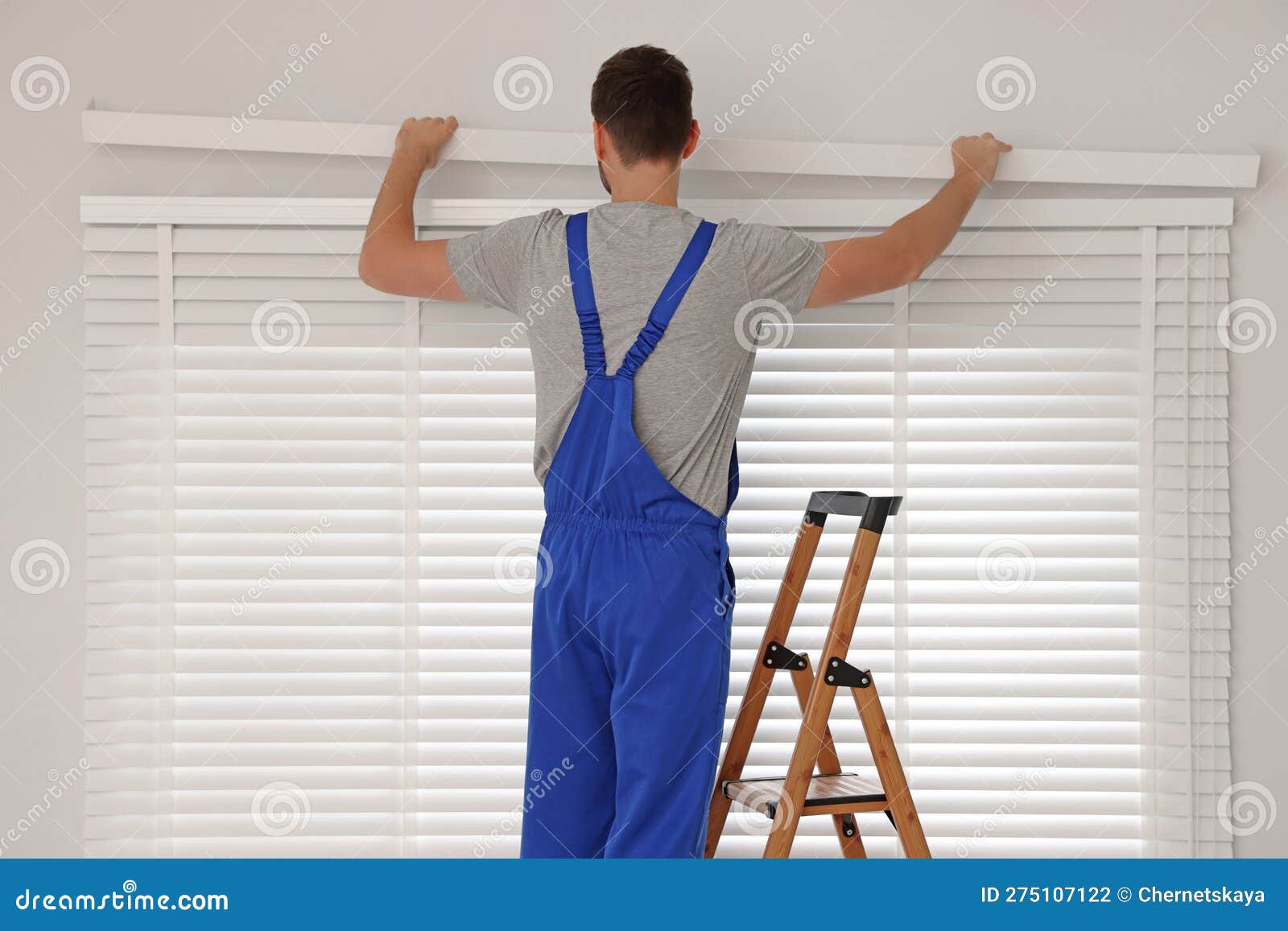 Worker in Uniform Installing Horizontal Window Blinds on Stepladder
