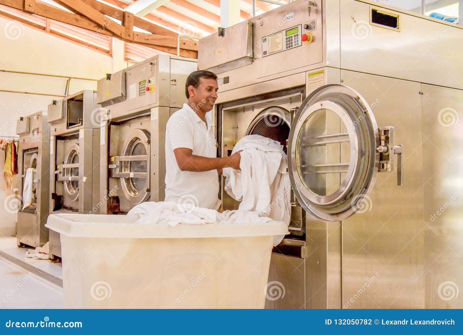 Worker in Uniform Putting Bed Sheet into Washing Machine Editorial