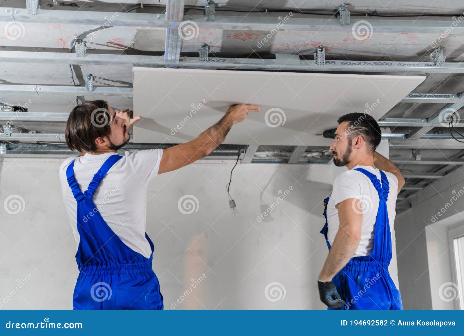 Workers in Blue Overalls Making Ceiling in Apartment Room Stock Photo