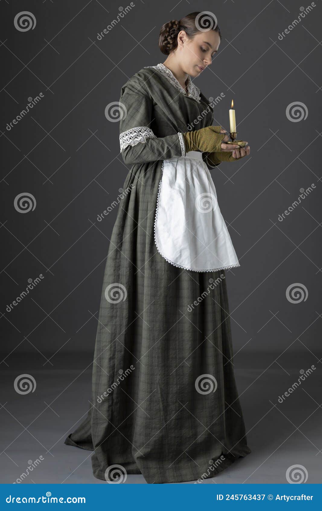 a working class victorian woman wearing a dark green check bodice and skirt with an apron and holding a candle.