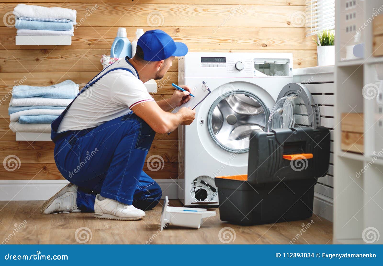 Working Man Plumber Repairs Washing Machine in Laundry Stock Photo