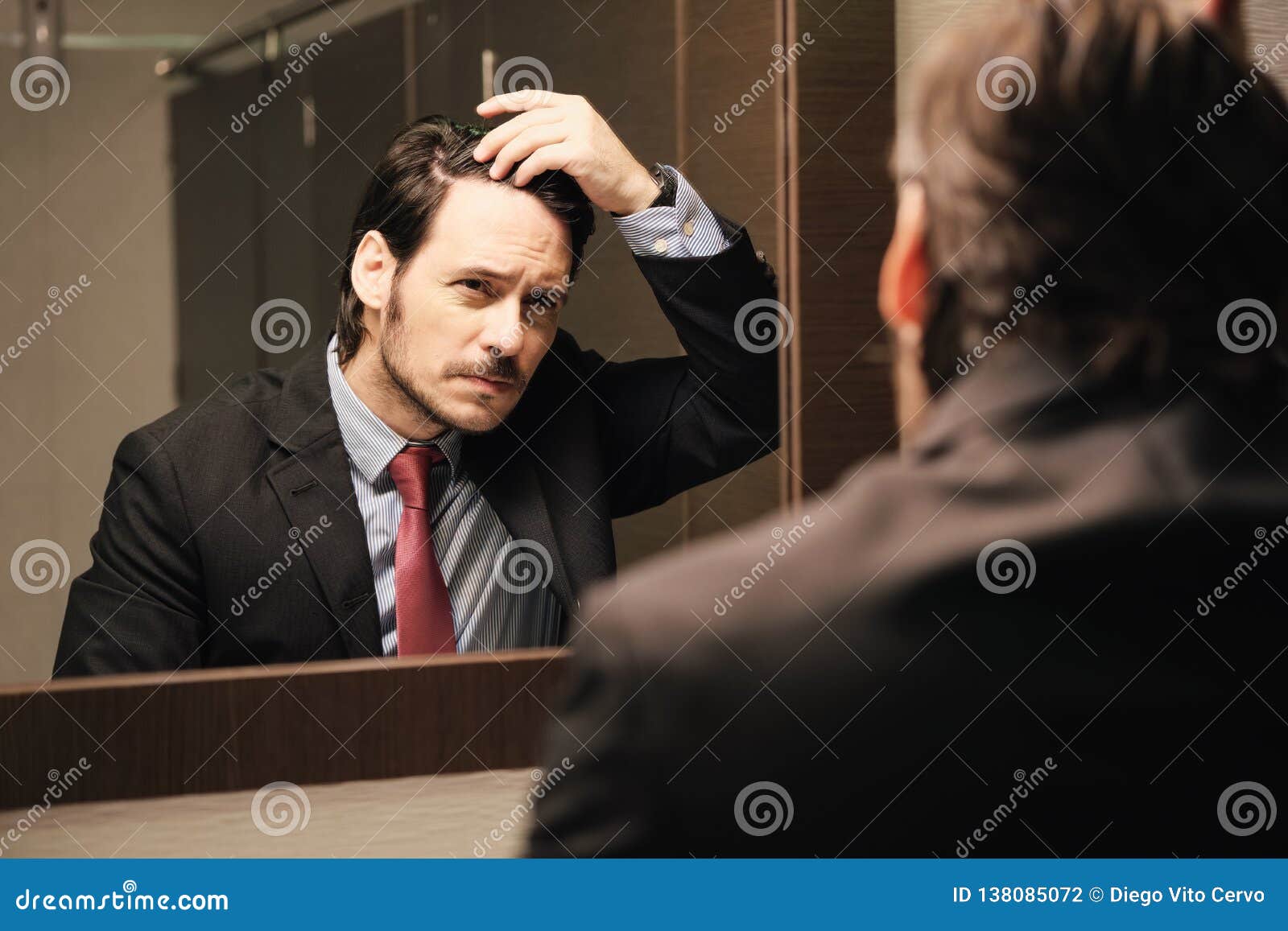 worried hispanic business man looking at hairline in office restrooms