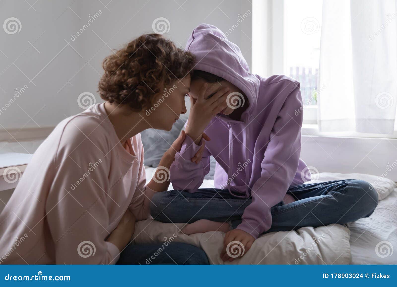 worried mom comforting depressed teen daughter crying at home