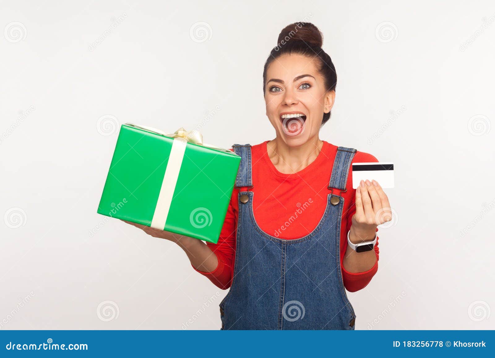 wow, credit for holiday gift purchase! portrait of stylish joyful girl in denim overalls holding present box and bank card