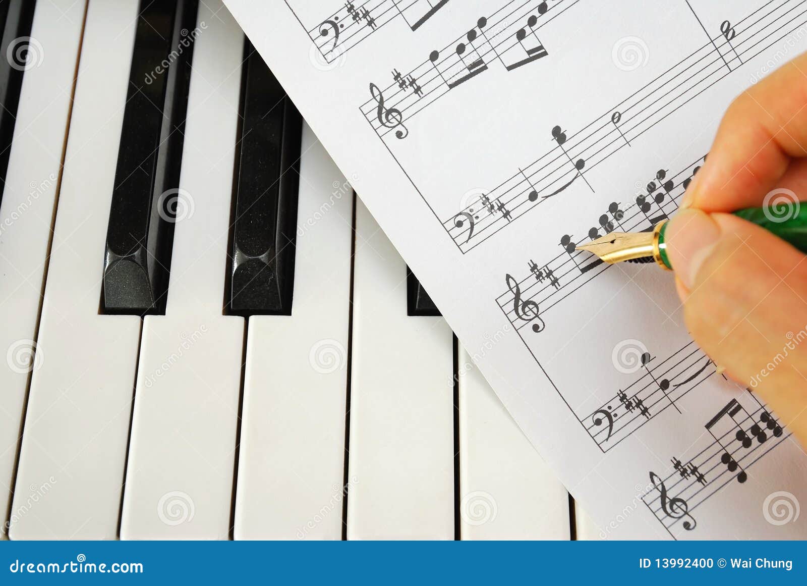 Writing on Music Score with Pen on Piano Keyboard Stock Photo