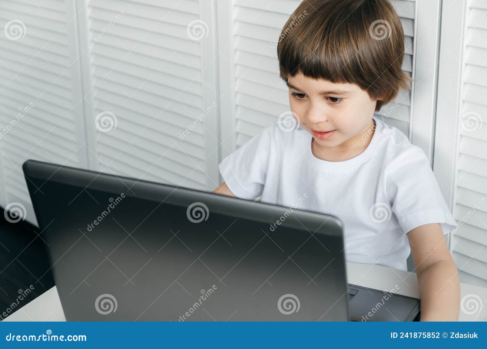 5 Year Boy Sit at the Table, Uses Laptop, Looking at the Screen. Child is Doing Homework Lesson