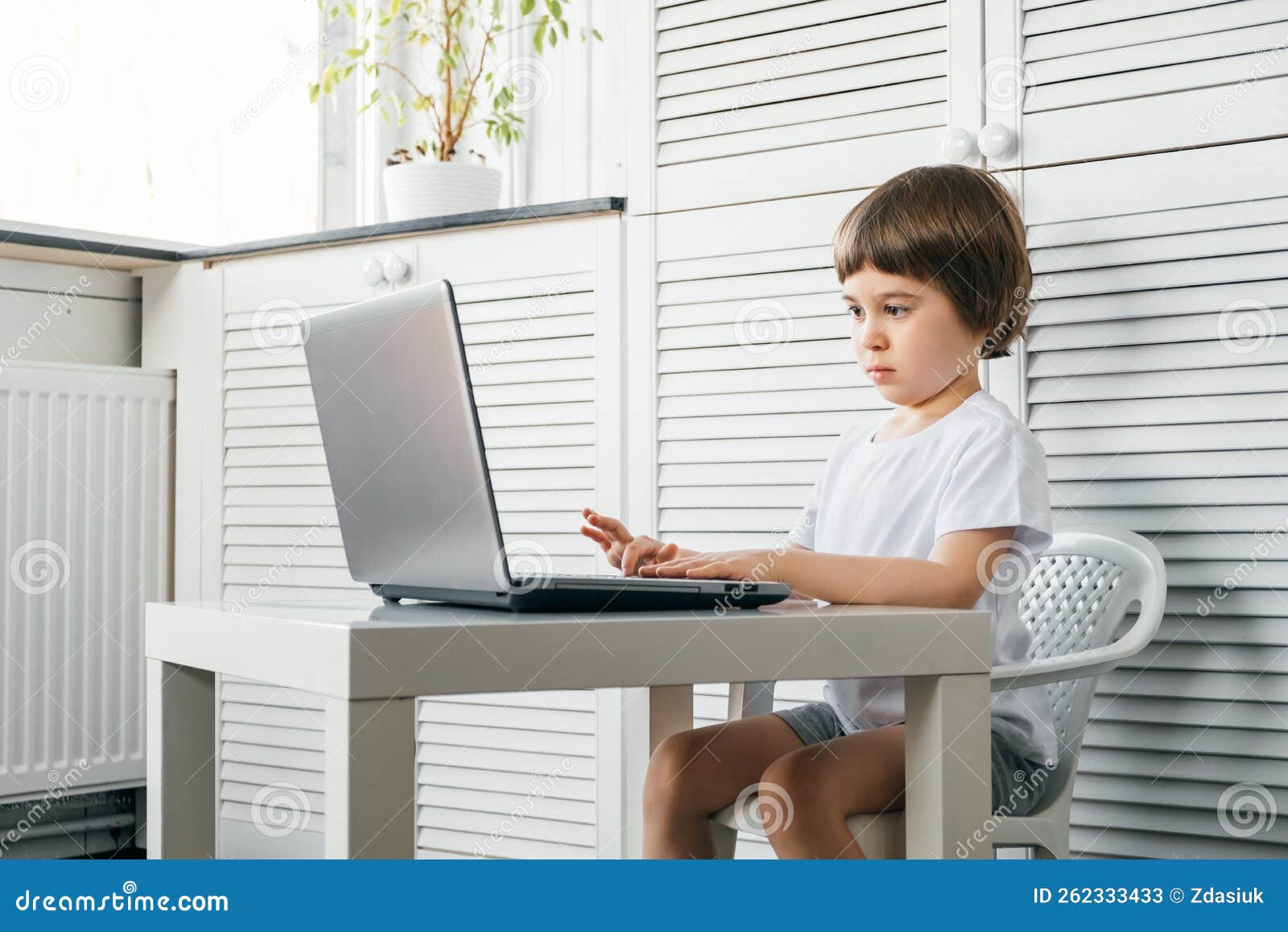 5 Year Boy Sit at the Table Uses Laptop and Looks at the Screen. Child is Doing Homework Lesson