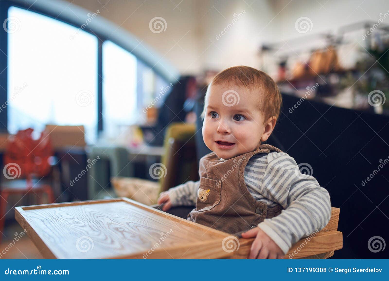 1 Year Old Baby Boy Sitting In Wooden High Chair At Home Stock