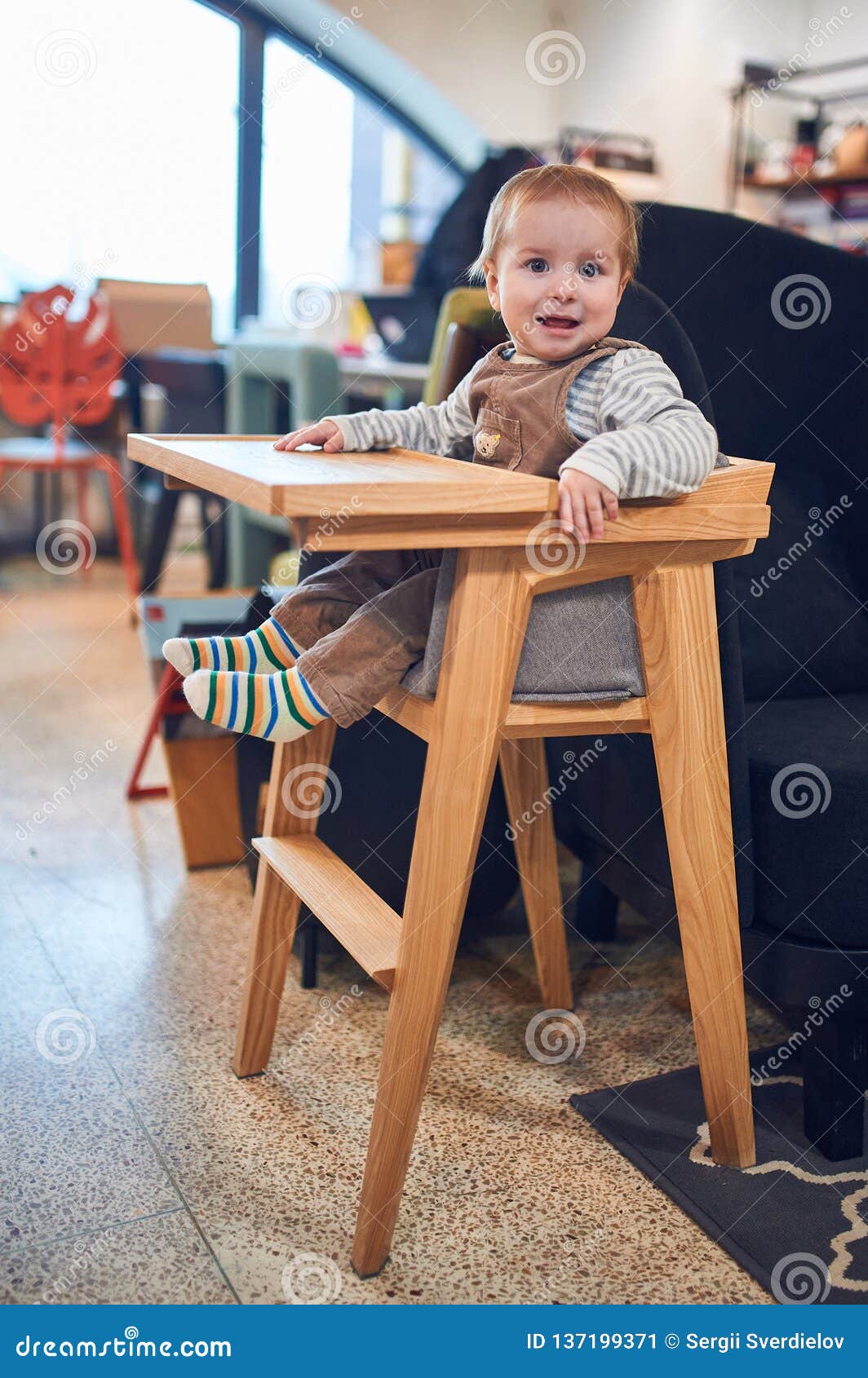 1 Year Old Baby Boy Sitting In Wooden High Chair At Home Stock