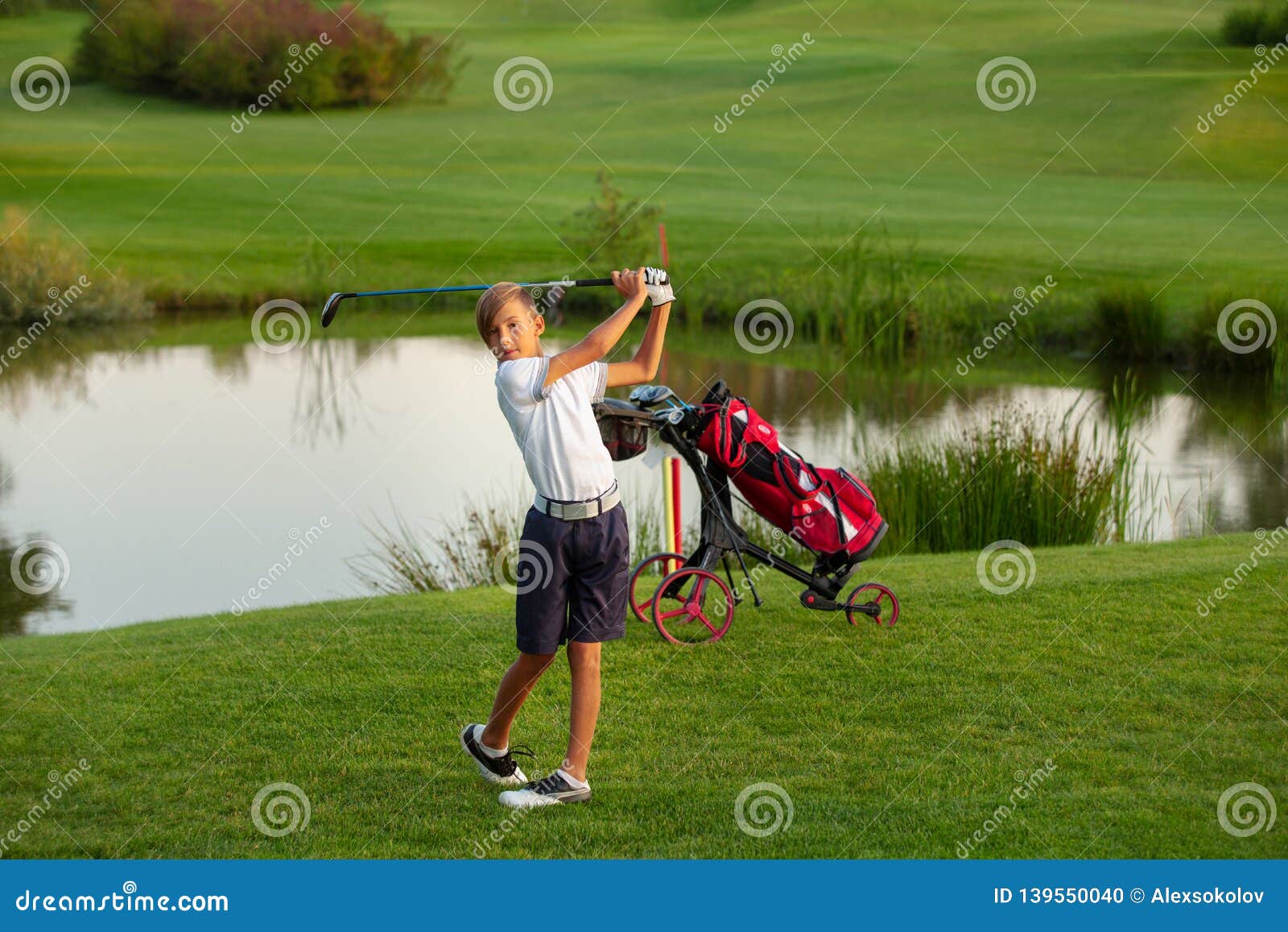 11 years old boy golfer playing golf near a lake. 11 years old boy golfer is hitting on golf course near a lake