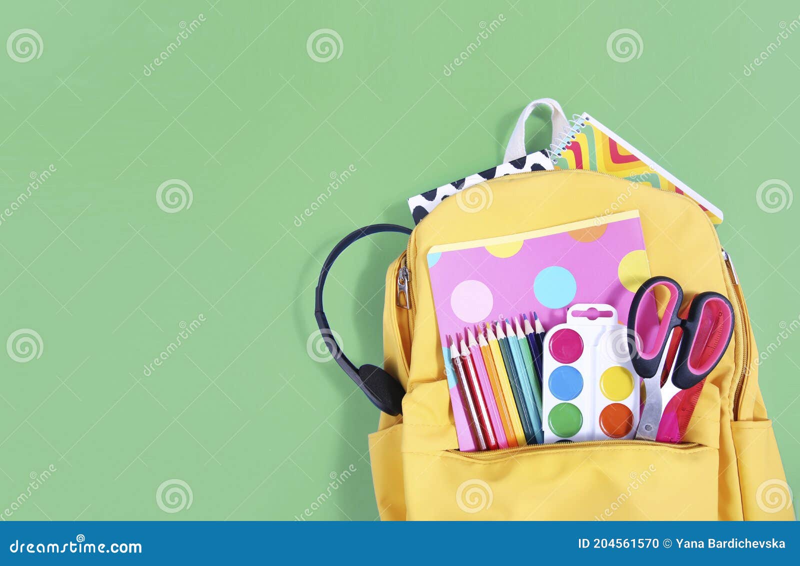 yellow backpack with school supplies on green background empty copy space.back to school advertisement .school accessories