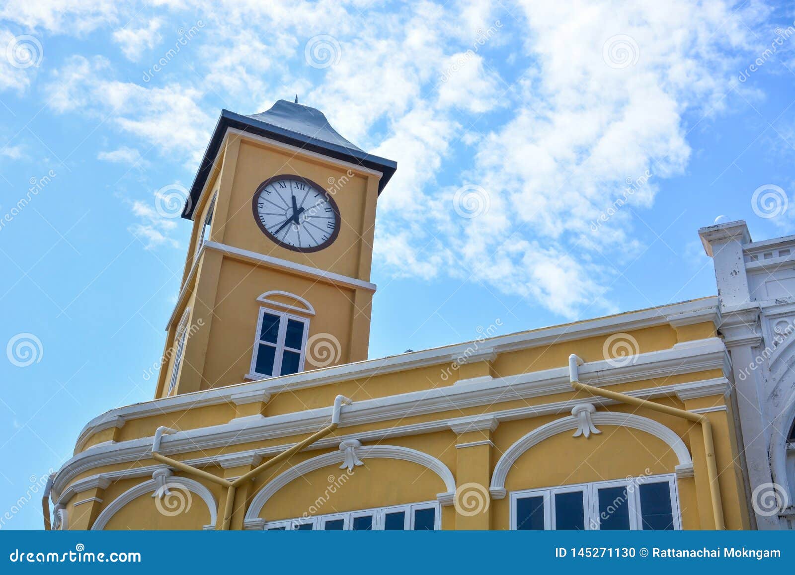 yellow building with clock tower in chino-portuguese style on blue sky background, phuket old town, thailand