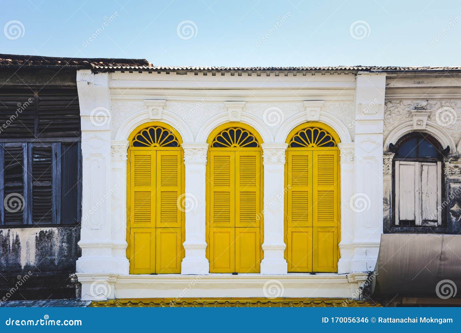 yellow color wooden arched window on white cement wall in chino portuguese style at phuket old town, thailand