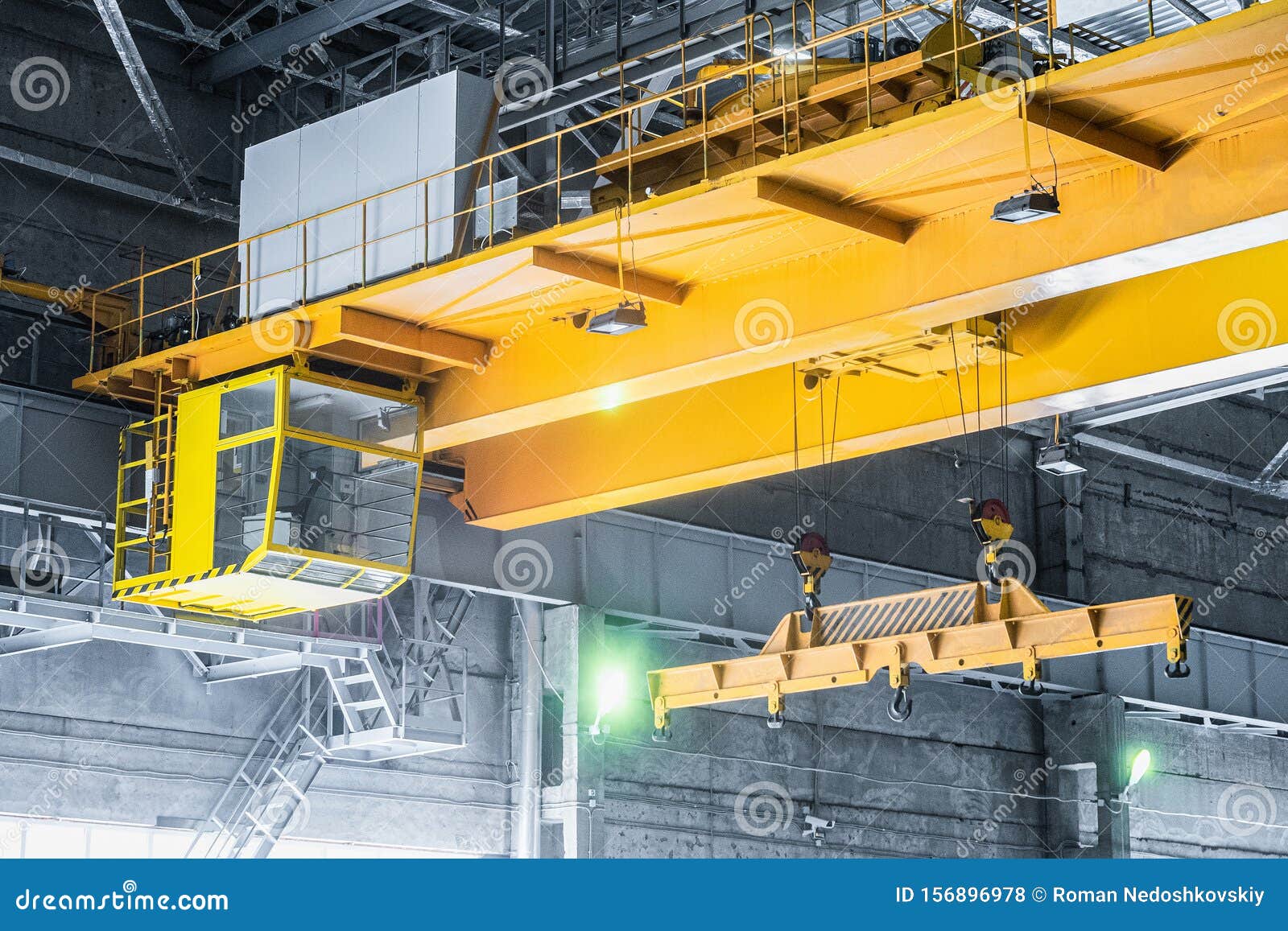 yellow overhead crane with linear traverse and hooks in engineering plant shop