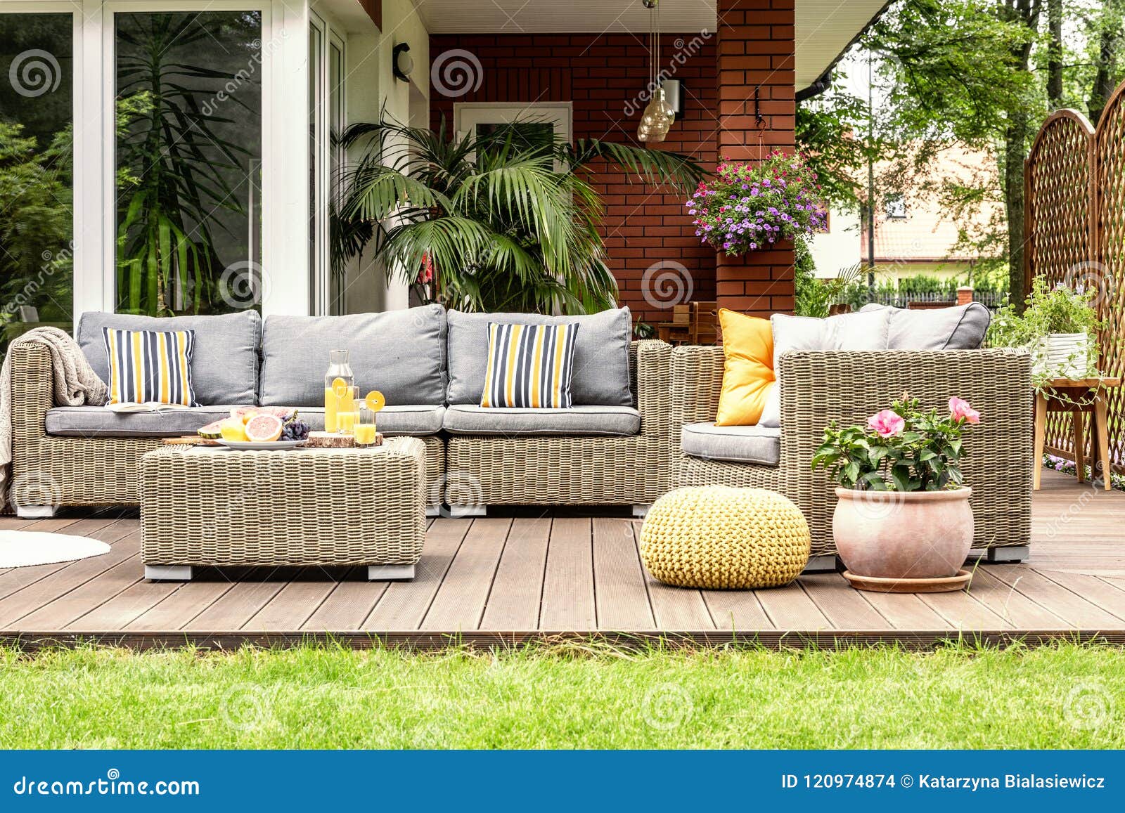 yellow pouf and flowers next to rattan garden furniture on wooden terrace of house. real photo