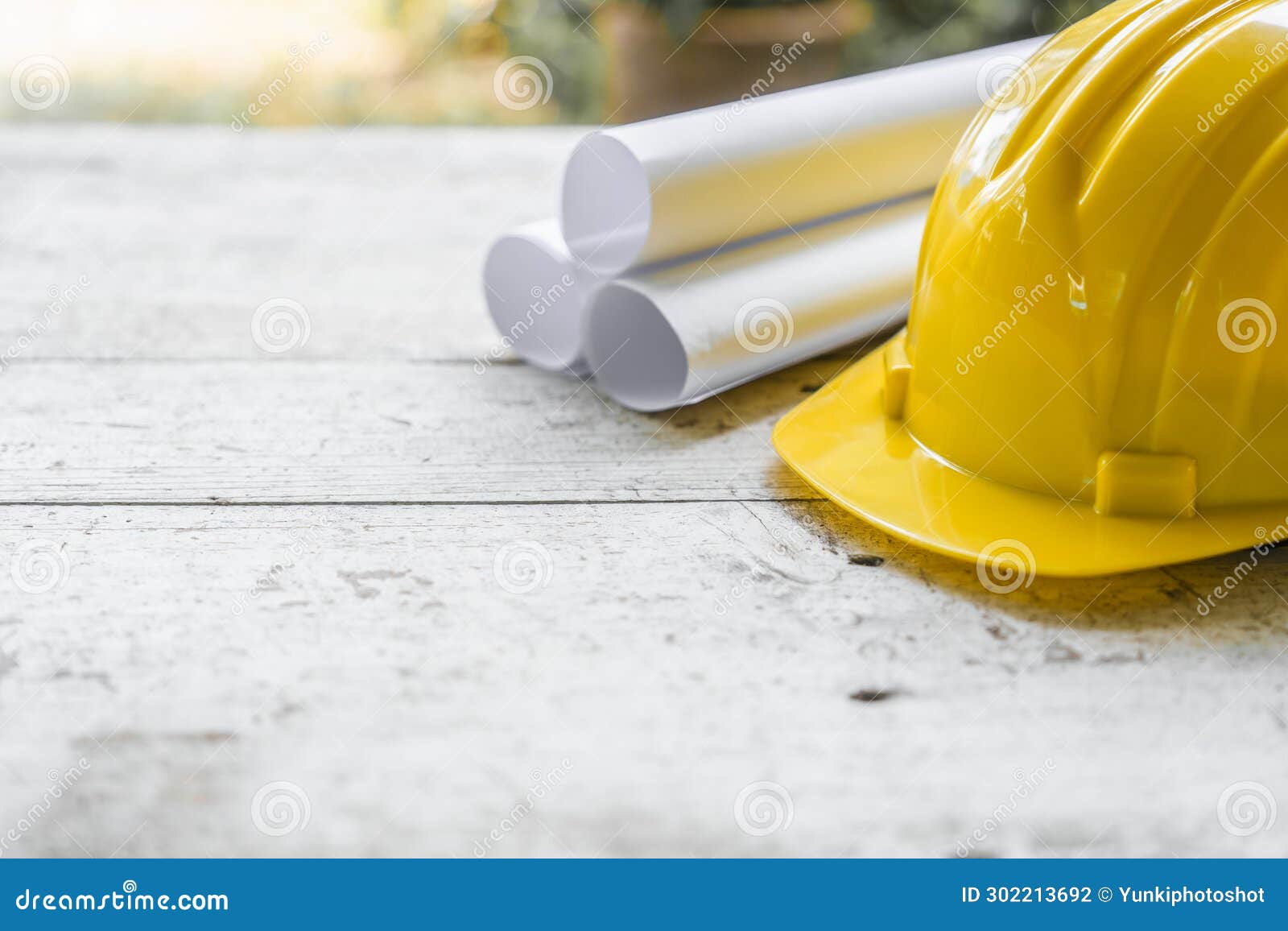 yellow safety helmet and rolled up architectural blueprints on a wooden desk