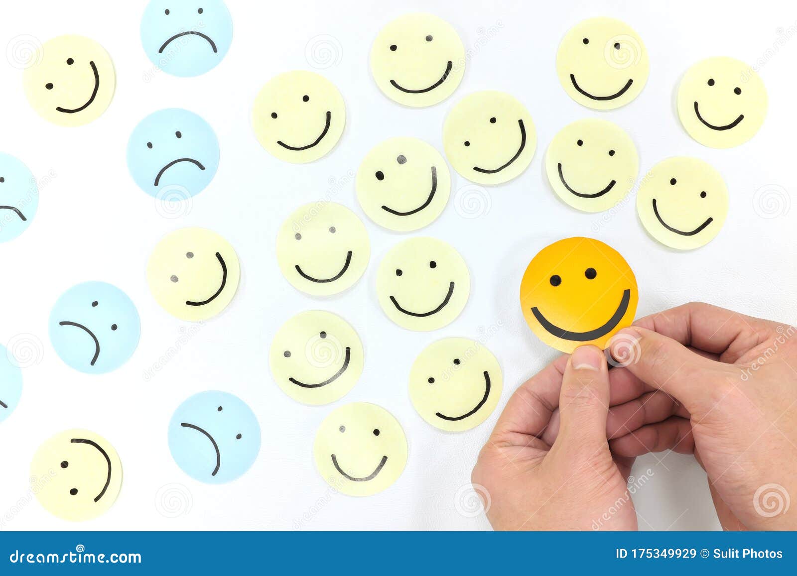 a yellow smiling face icon among a group of sad and happy face emoticons. positivity, attraction and happiness.