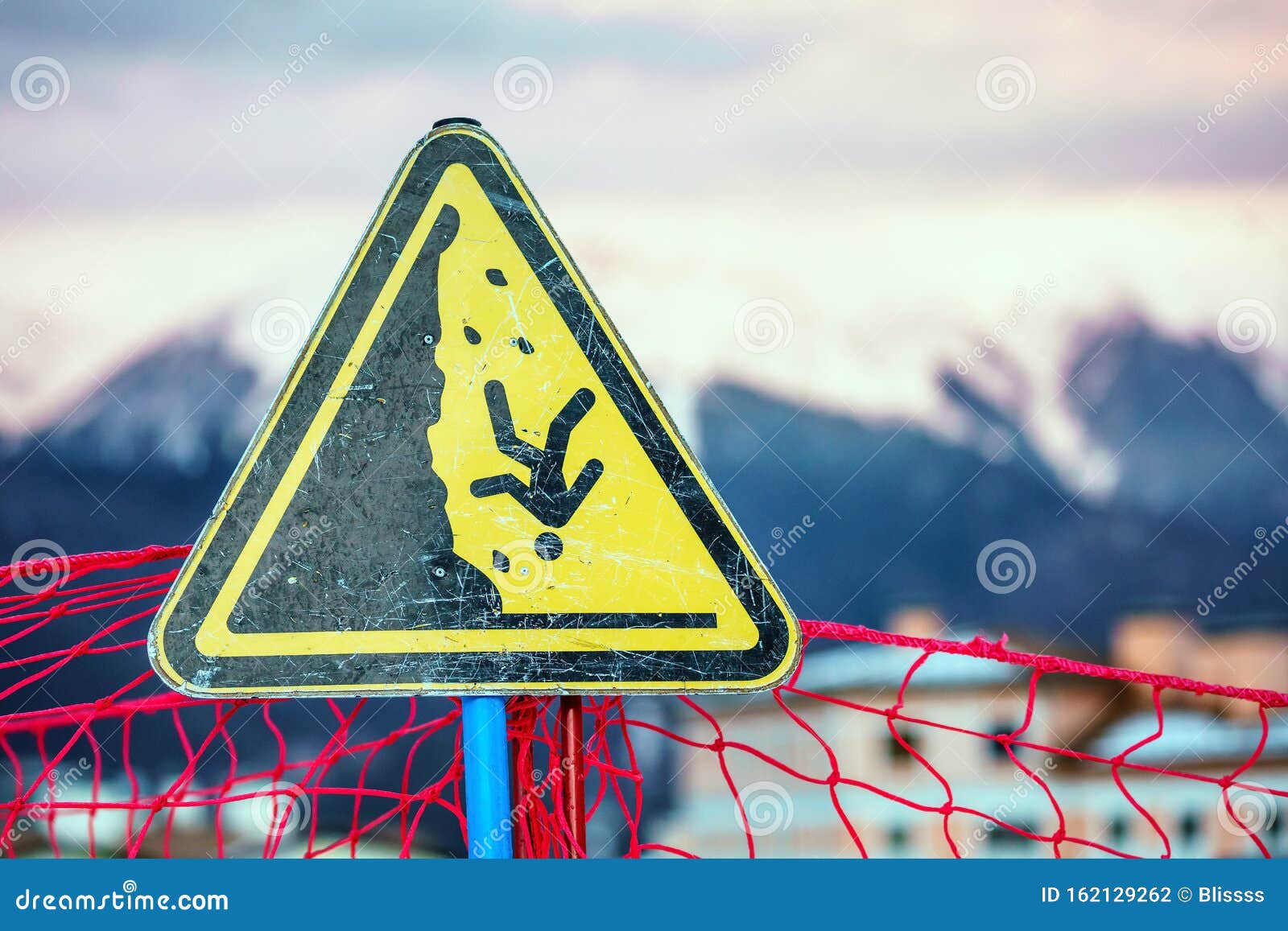 yellow triangle outdoor warning sign on snowy mountain peaks winter background displaying man falling down a steep as safety peril