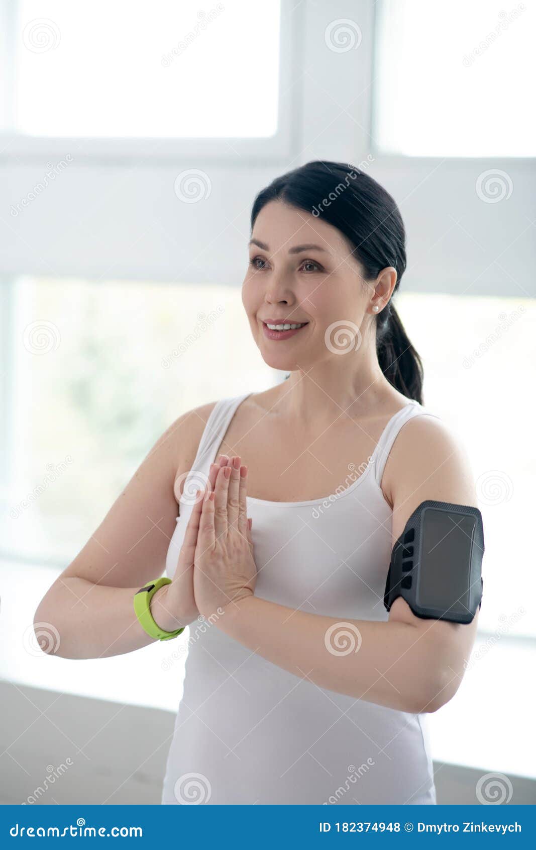 brunette female performing namaste, pressing hands together, wearing pulsometer