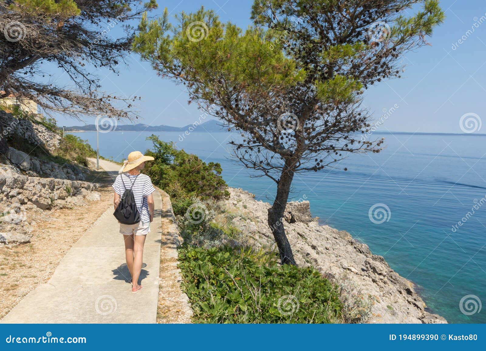 young active feamle tourist wearing small backpack walking on coastal path among pine trees looking for remote cove to