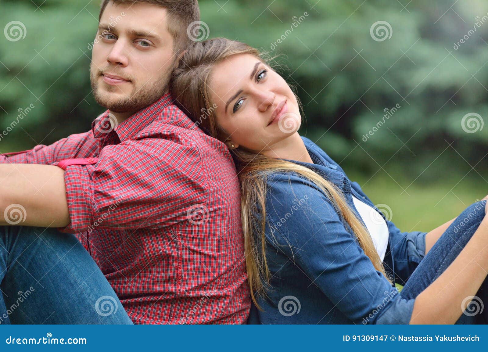 young adult couple siting back in back in nature