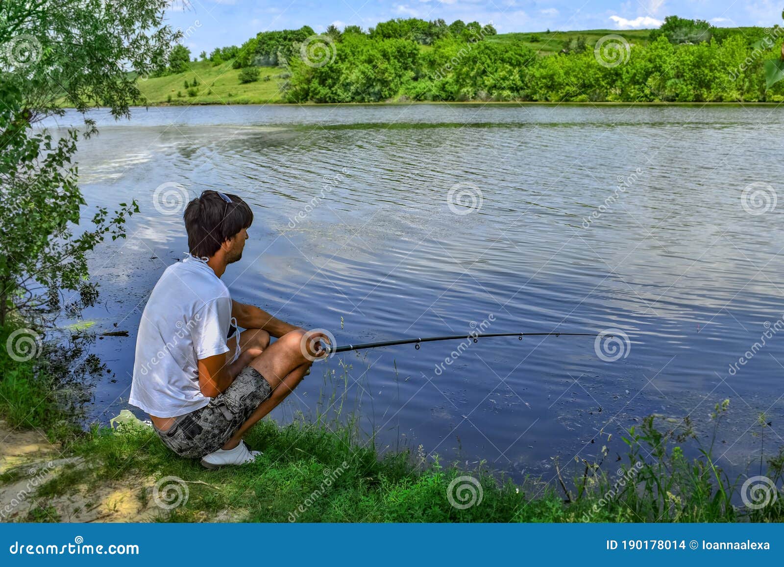 Young Adult Man Catches Fish with Fishing Rod Sitting on the Shore