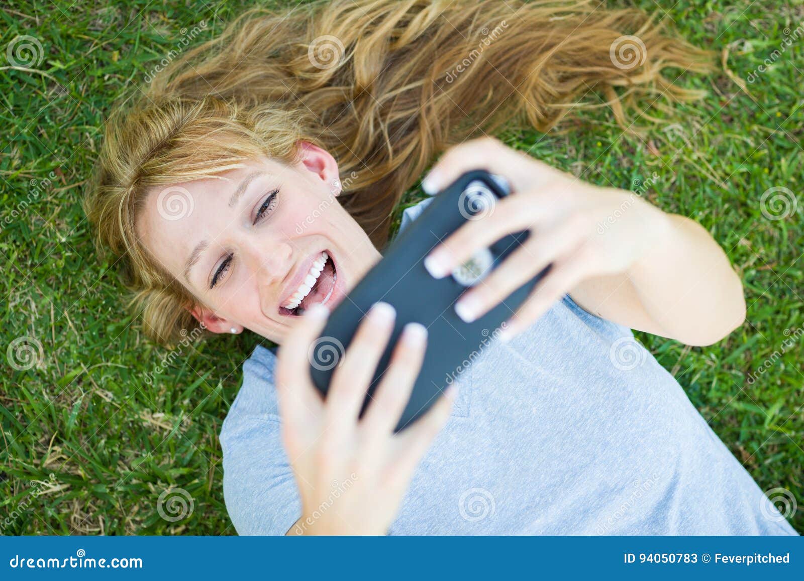 Young Adult Woman Laying in Grass Taking Selfie on Smart Phone.