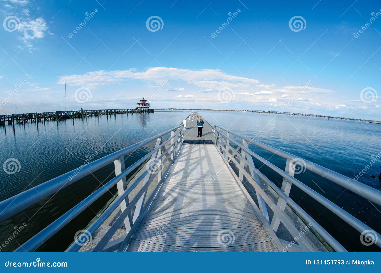 young adult woman walks out onto a pier near the choptank river lighthouse in cambridge maryland on a sunny spring day