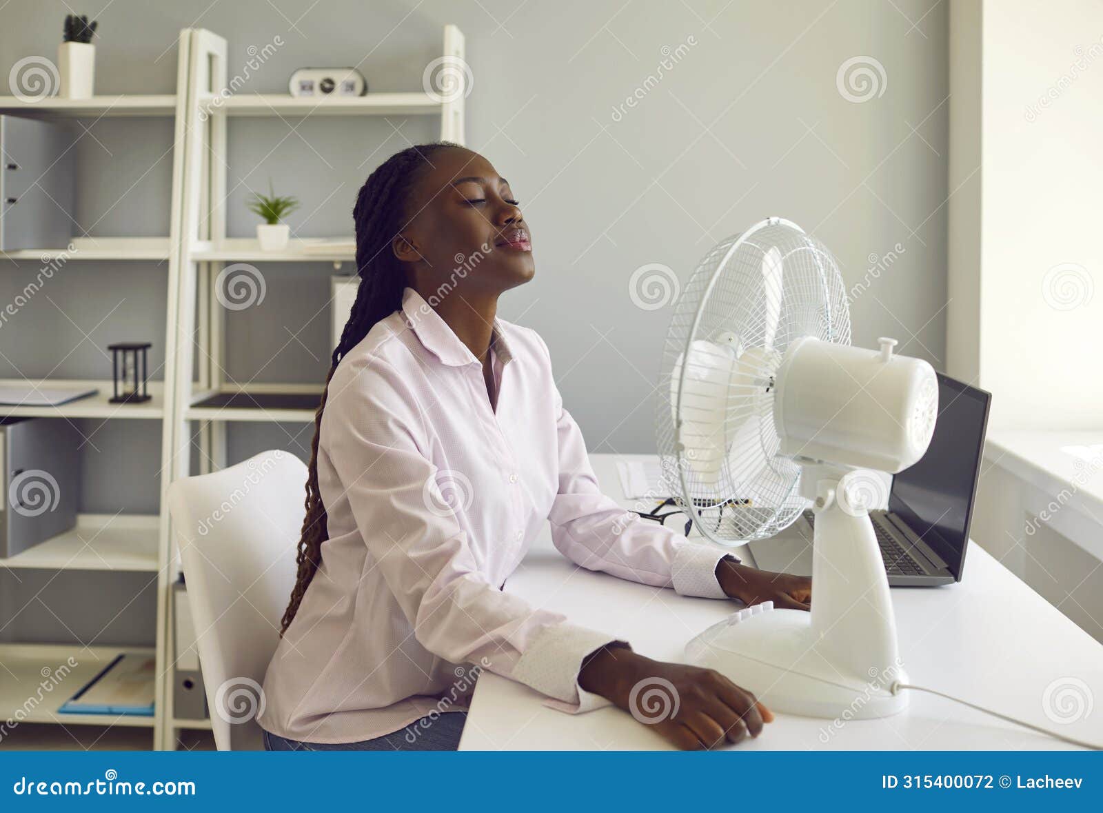 young african american woman working at office using electric fan during heatwave in office.