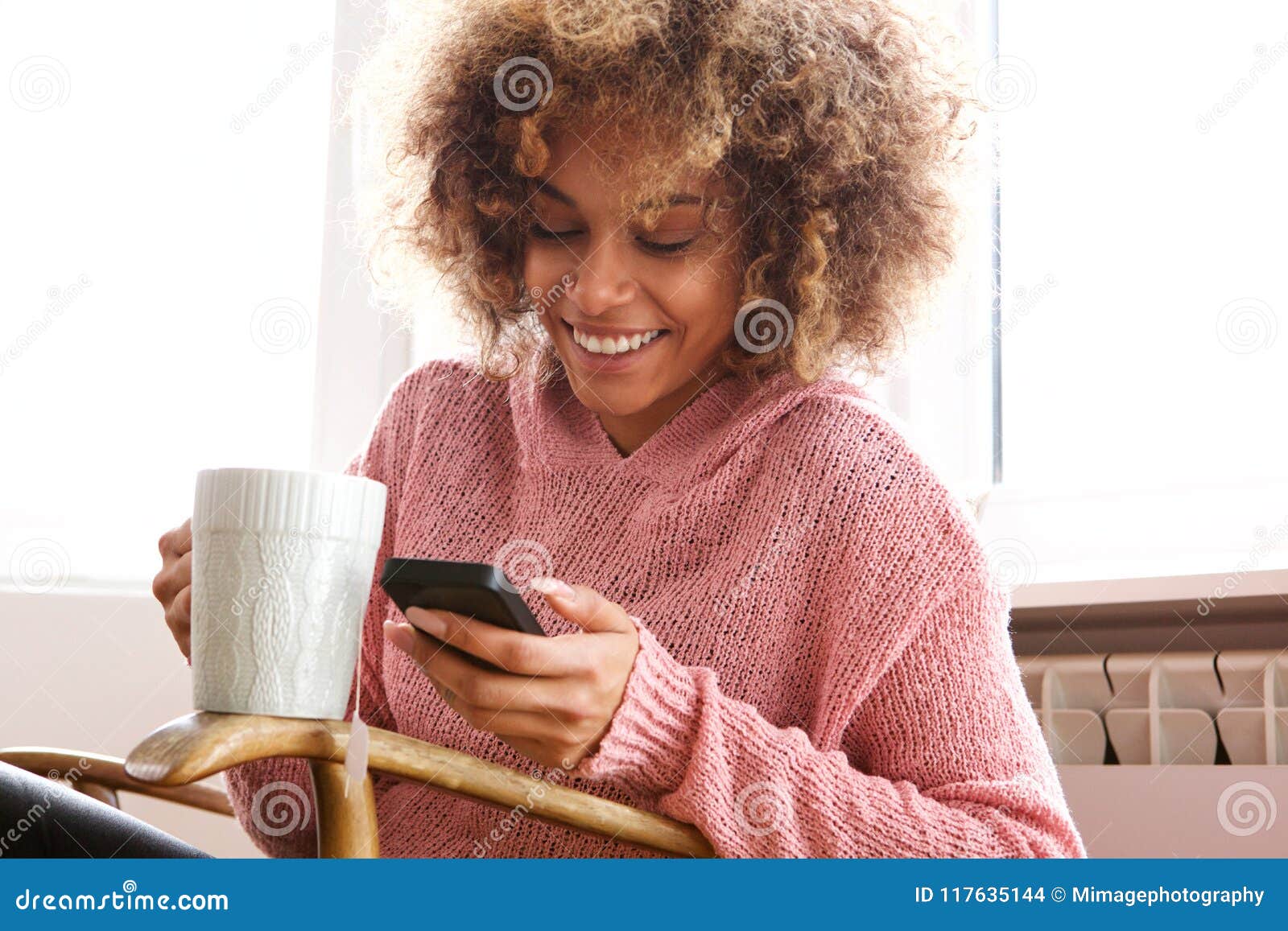 young african american woman drinking hot cup of coffee and looking at cellphone