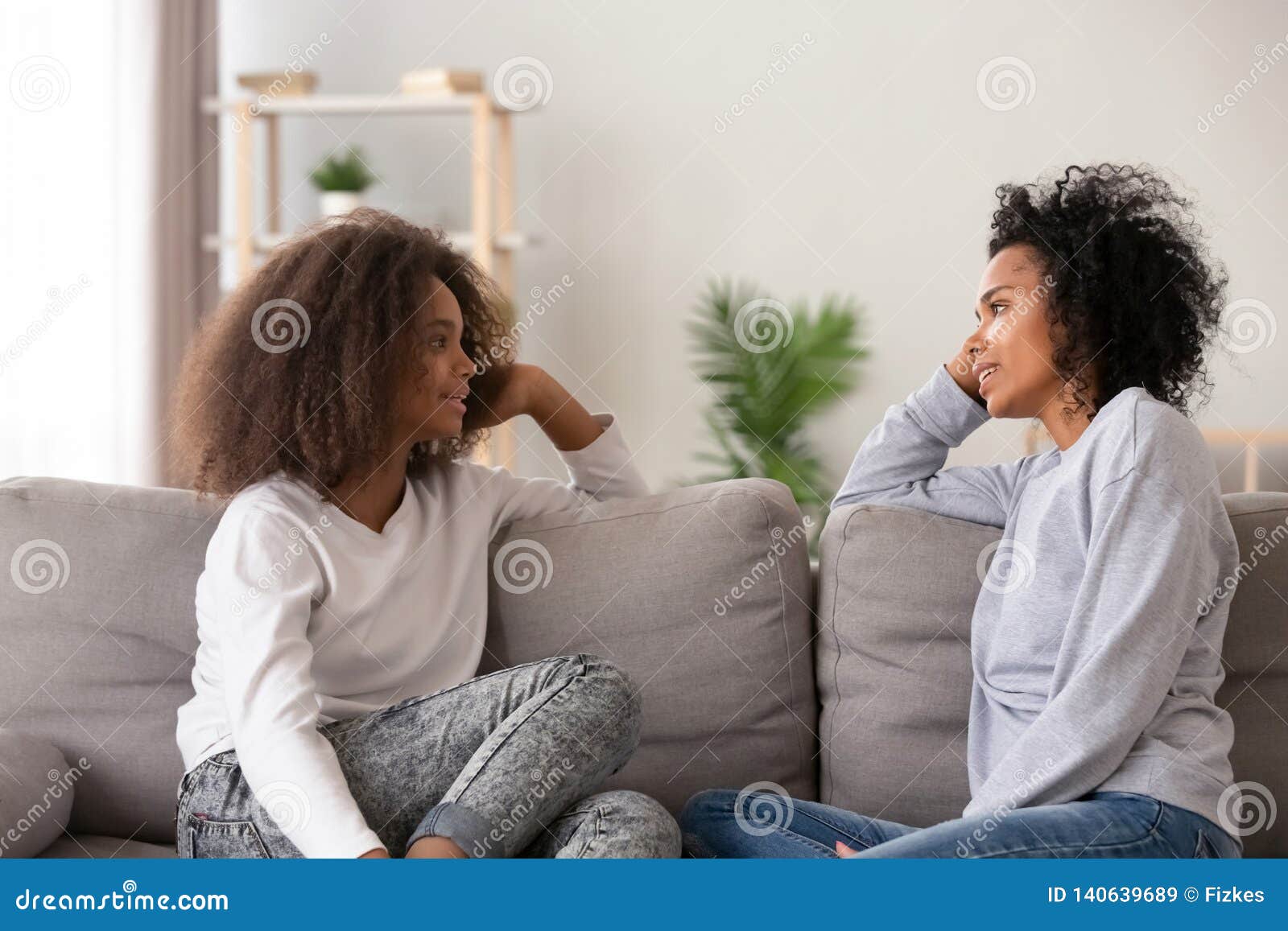 african young mom listening teen daughter sitting on couch together