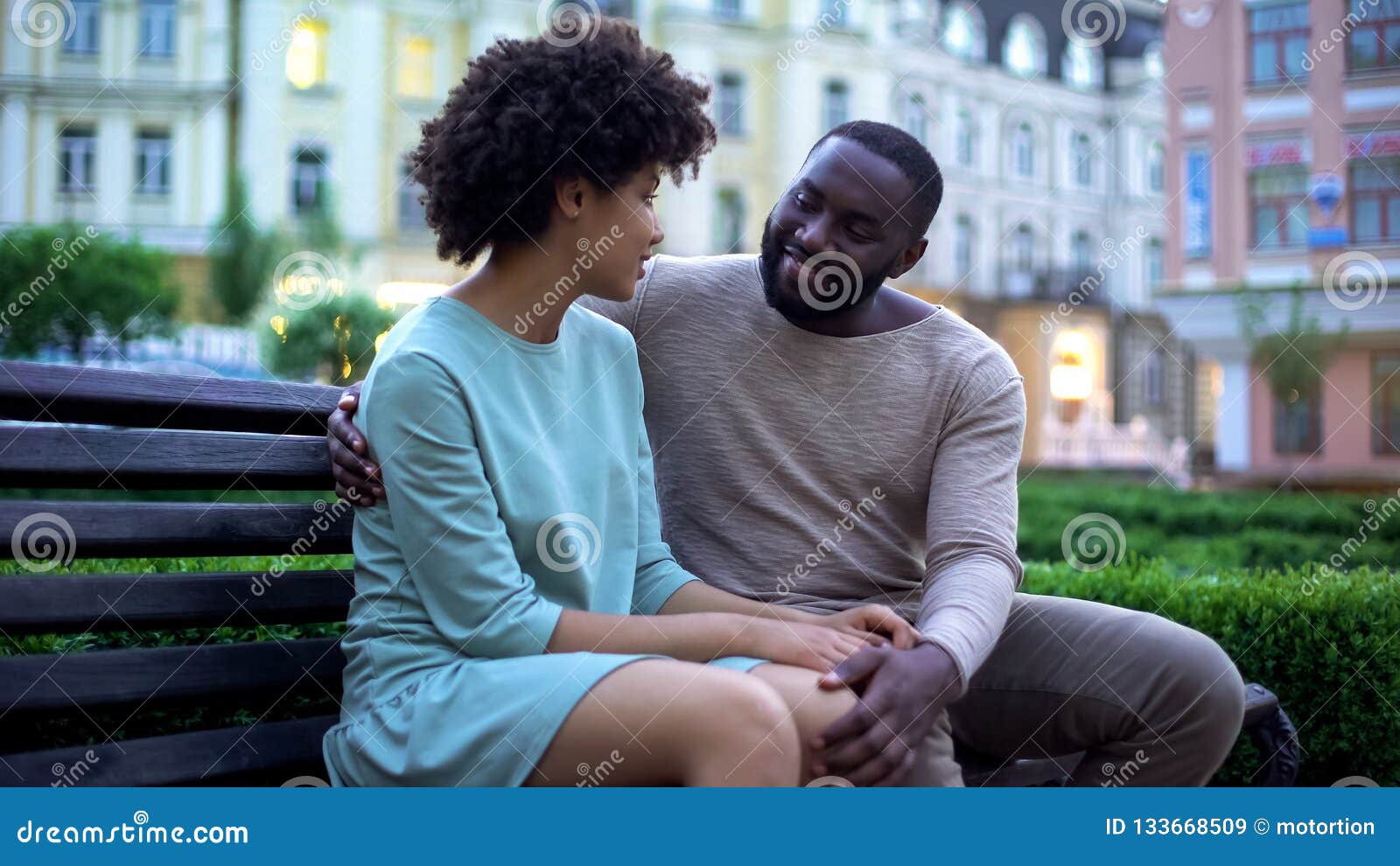 Young African Couple Cuddling On Bench At Sunset Date In City Park