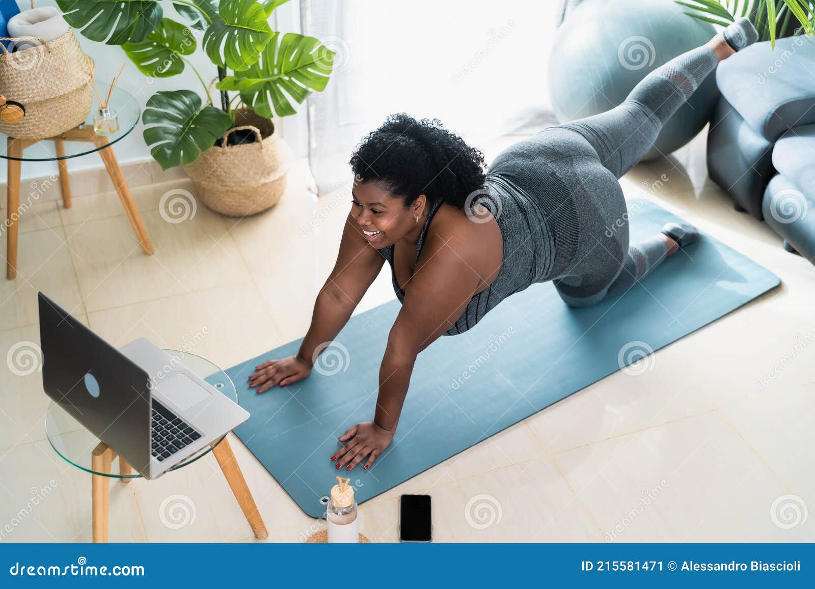 young african curvy woman doing pilates virtual fitness class with laptop at home