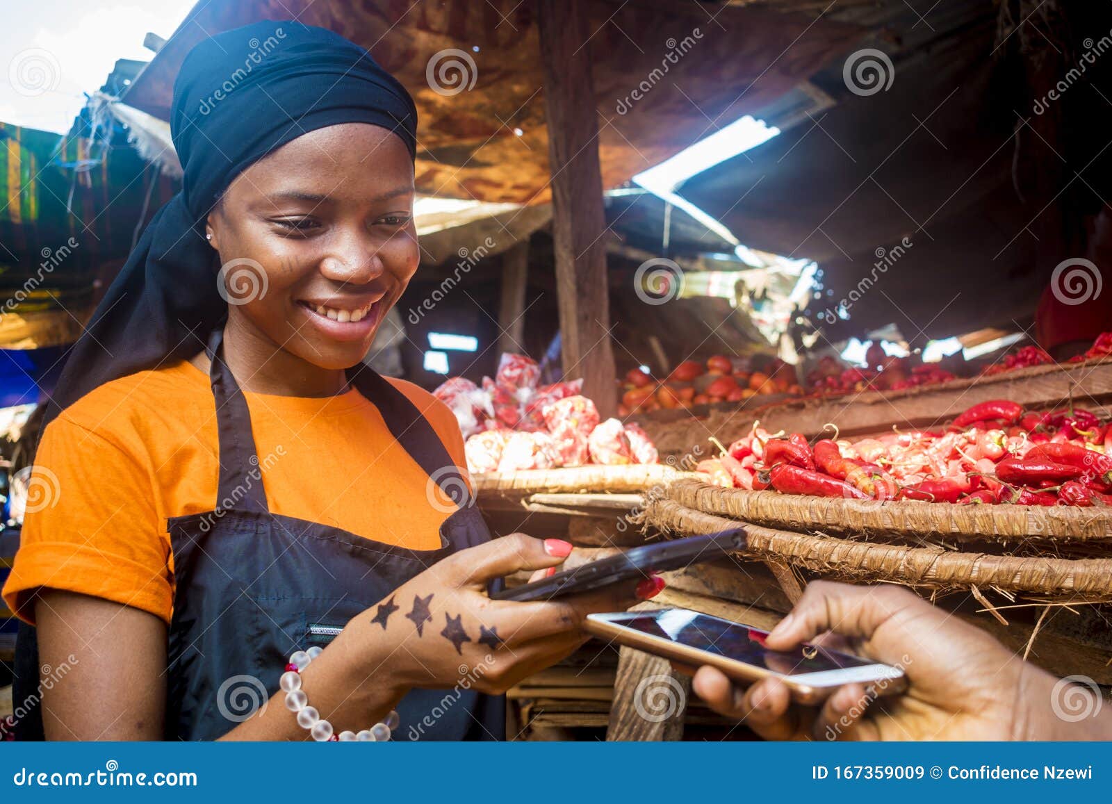 young black woman selling tomatoes in a local african market receiving payment via mobile phone transfer