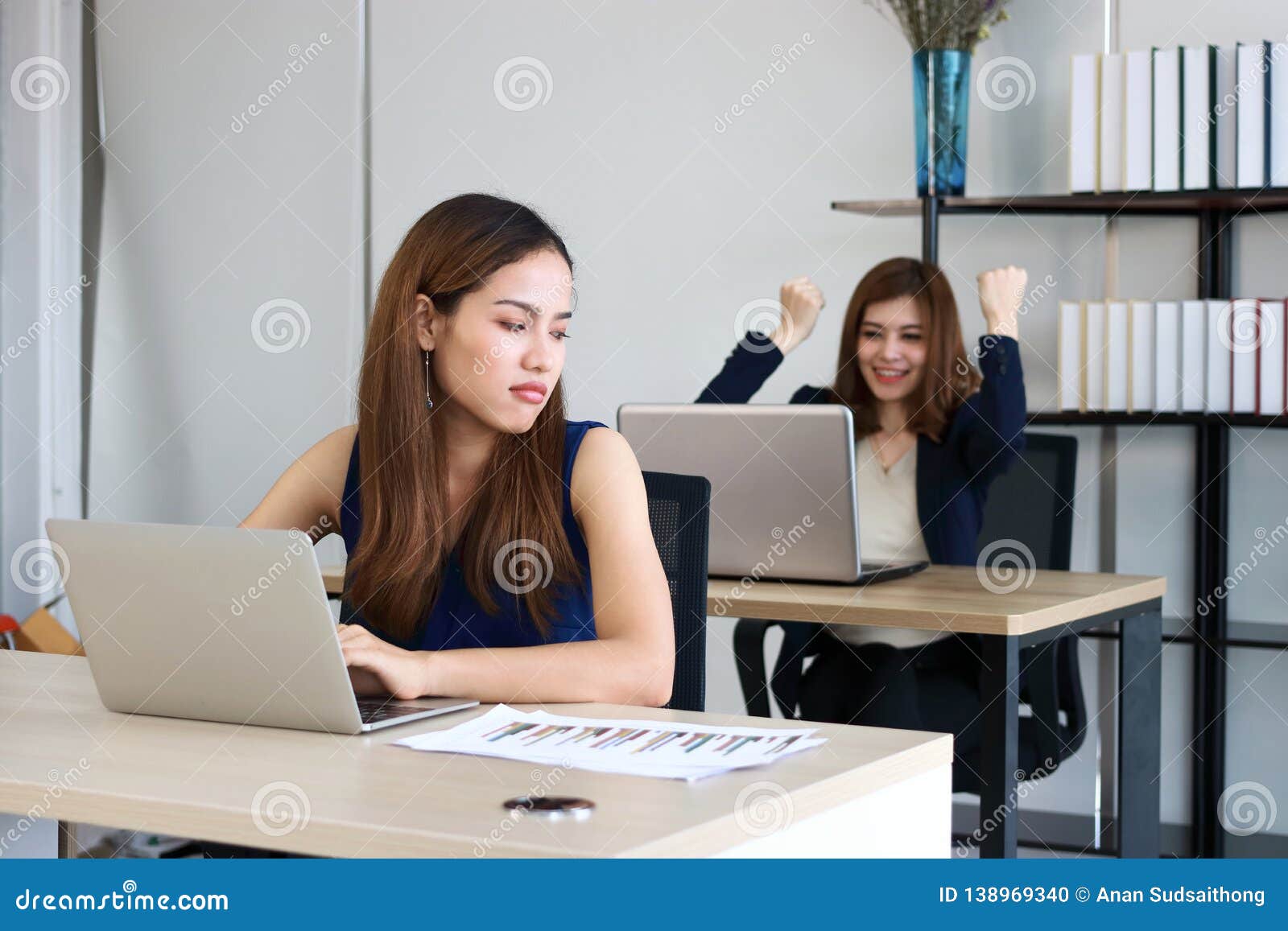 young angry envious asian business woman looking successful competitor colleague in office