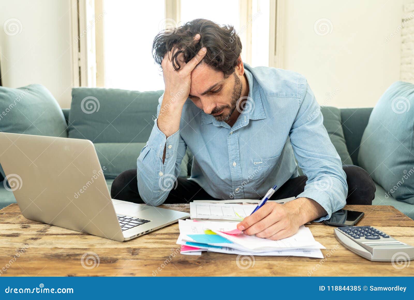 angry man paying bills as home with laptop and calculator