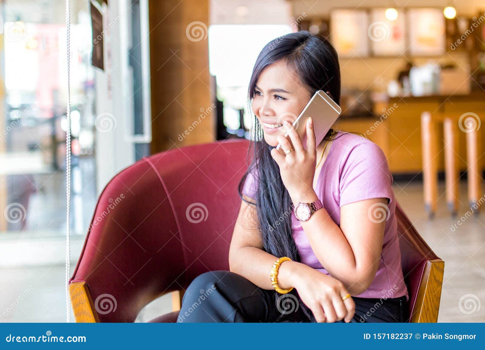 young asain woman smiling in cafee shop talking mobile phone and texting in social networks, sitting alone