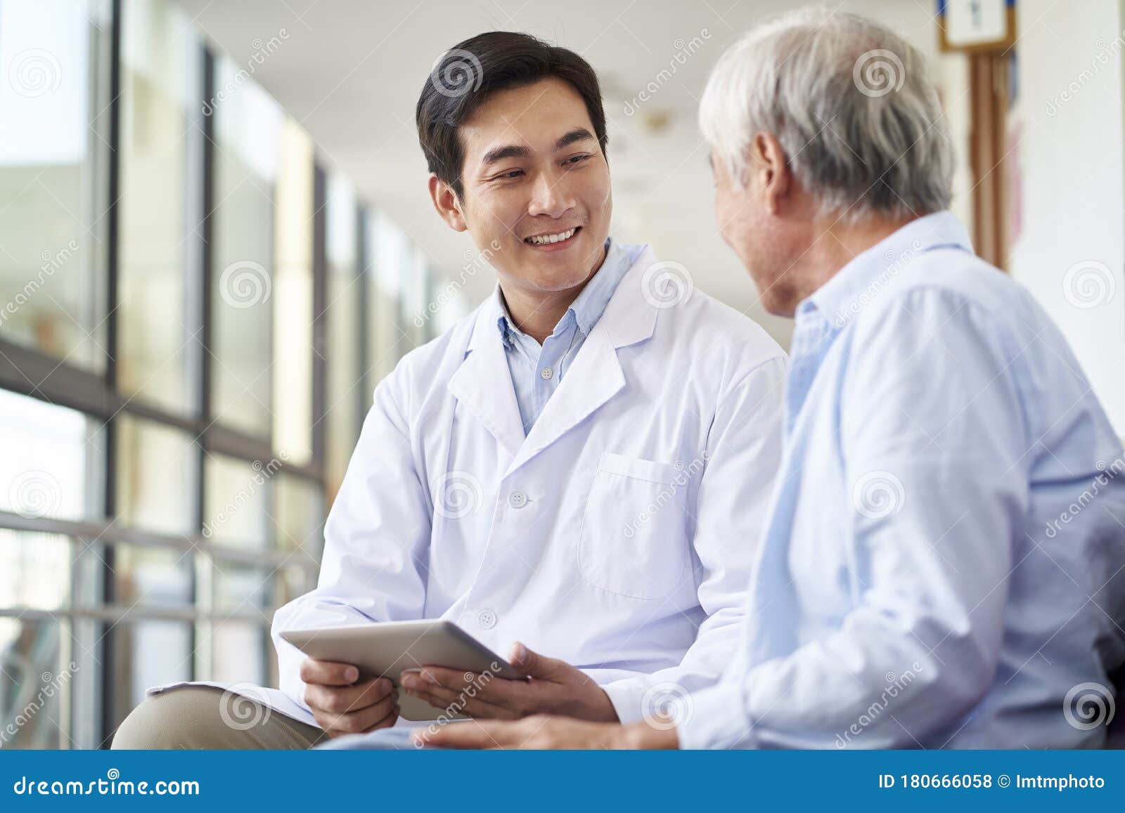 young asian doctor talking to senior man in hospital hallway