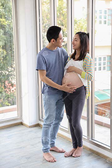 Young Asian Husband Standing And Embracing Eyes Contract Together With Young Asian Pregnant 