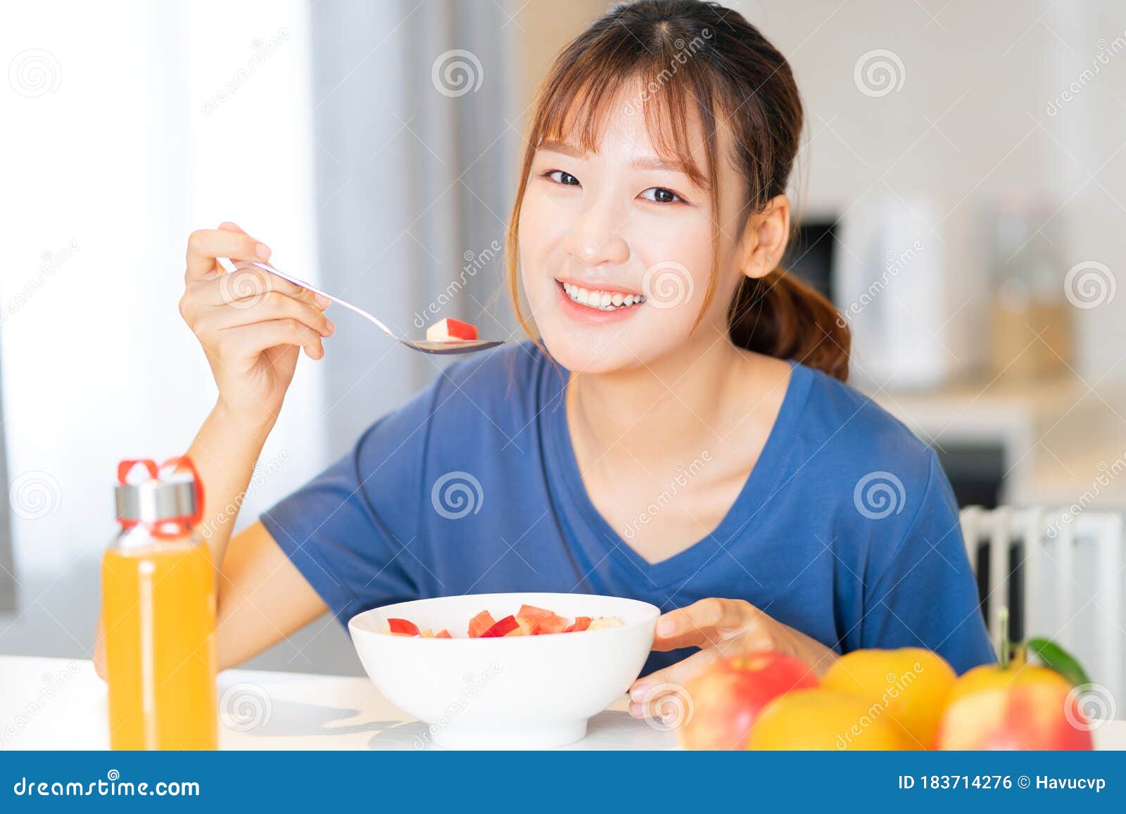 A Young Asian Woman Eating Breakfast with Fruit in Her Kitchen Stock