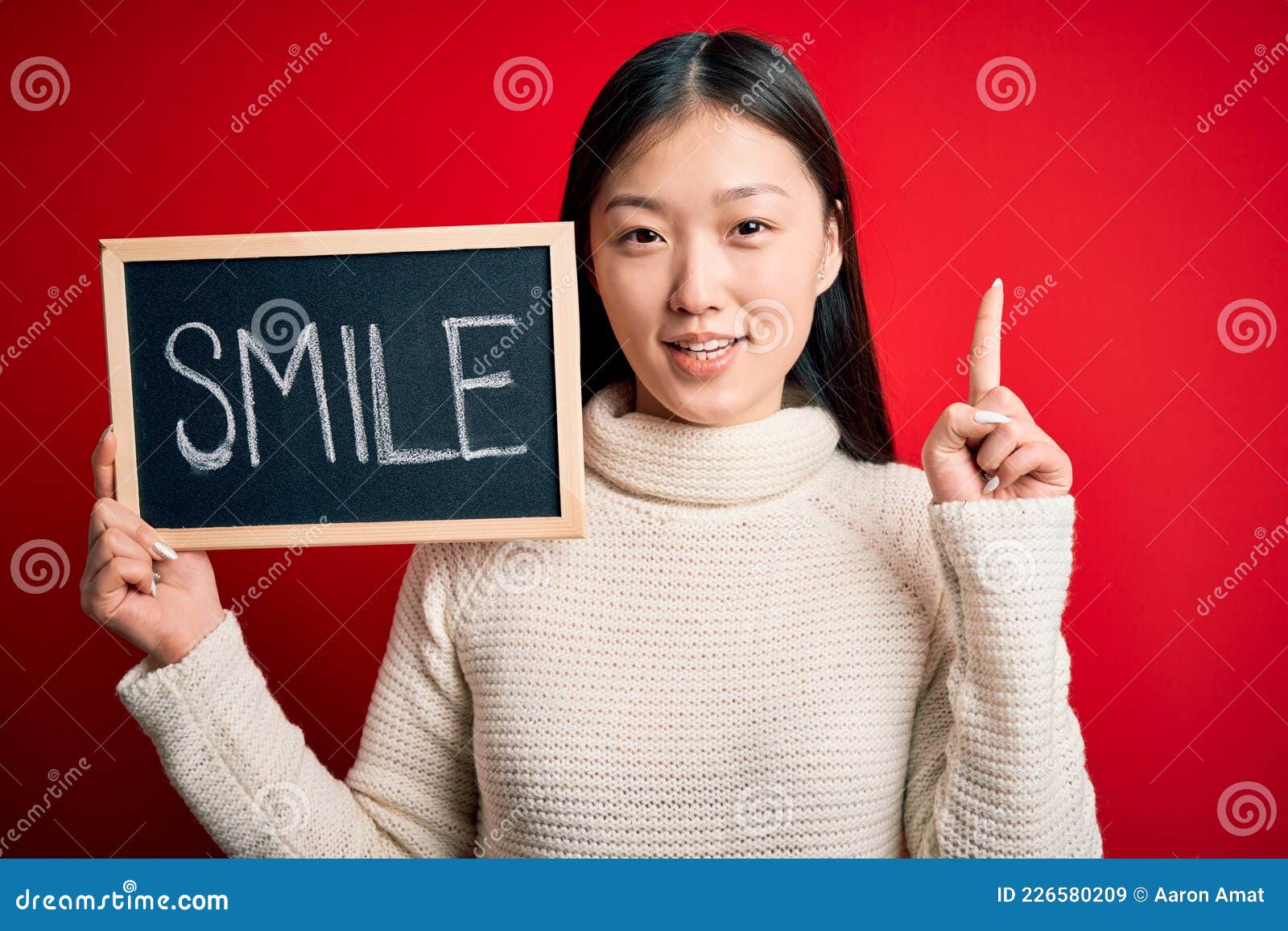 young asian woman holding blackboard with smile word as hapinness message surprised with an idea or question pointing finger with