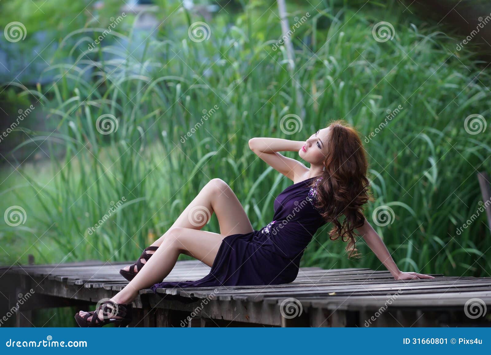 Young Asian woman posing in greenery background. Young beautiful Asian woman in violet evening dress sitting on wooden bridge in the greenery background, model is Thai Ethnicity.