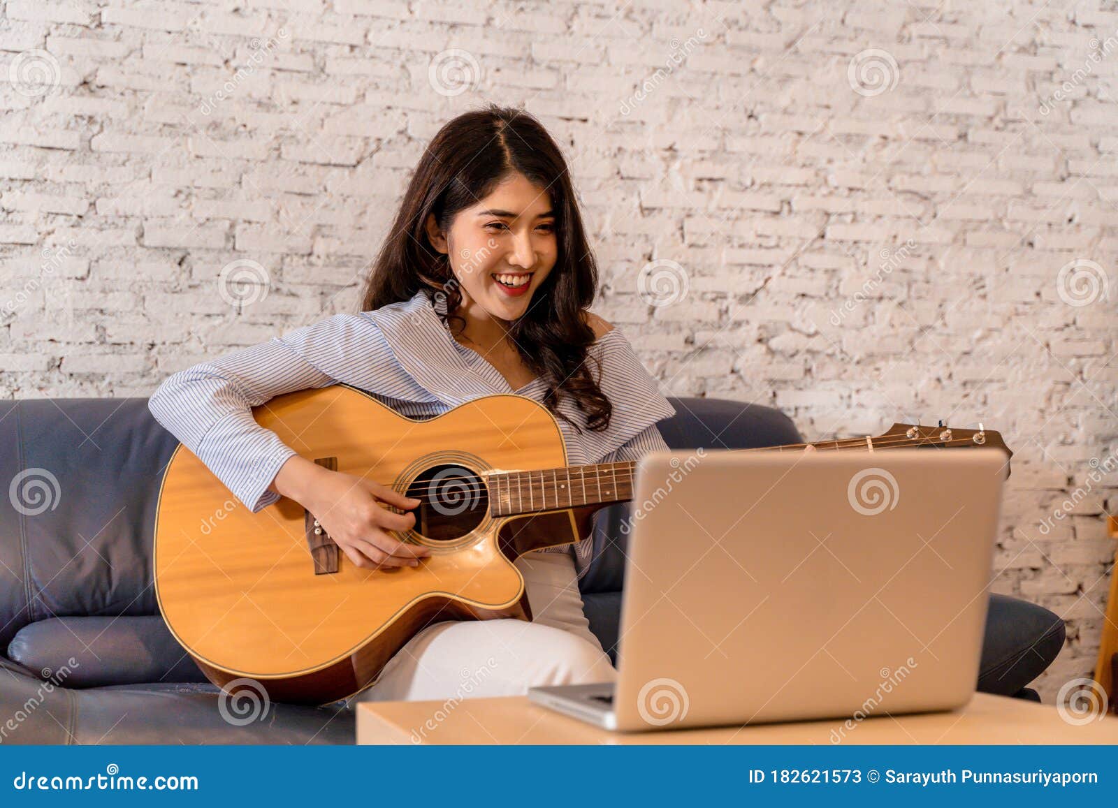 young asian woman practicing and learning how to play guitar on laptop computer monitor. female guitarist watching