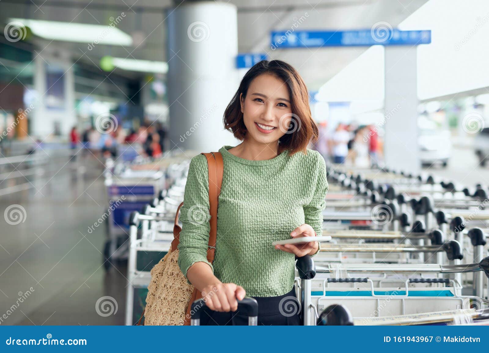 young asian woman waiting on the side of the street for her ride that she booked via a ride-hailing app