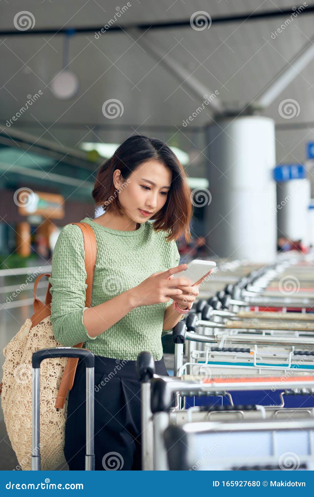 young asian woman waiting on the side of the street for her ride that she booked via a ride-hailing app