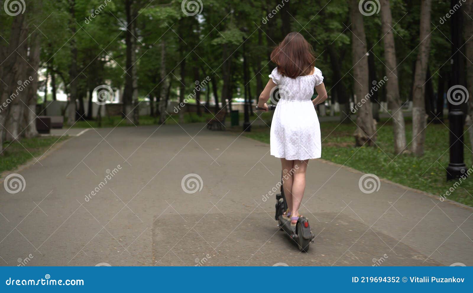 Young Asian Woman In A White Dress Rides A Sharing Electro Scooter In
